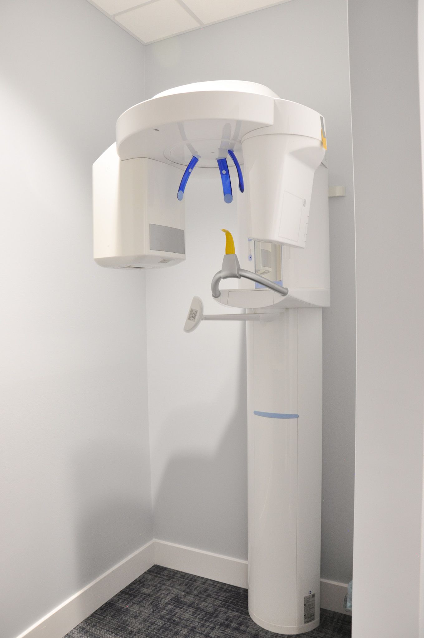 Dental panoramic X-ray machine in a white-walled room with dark carpet.