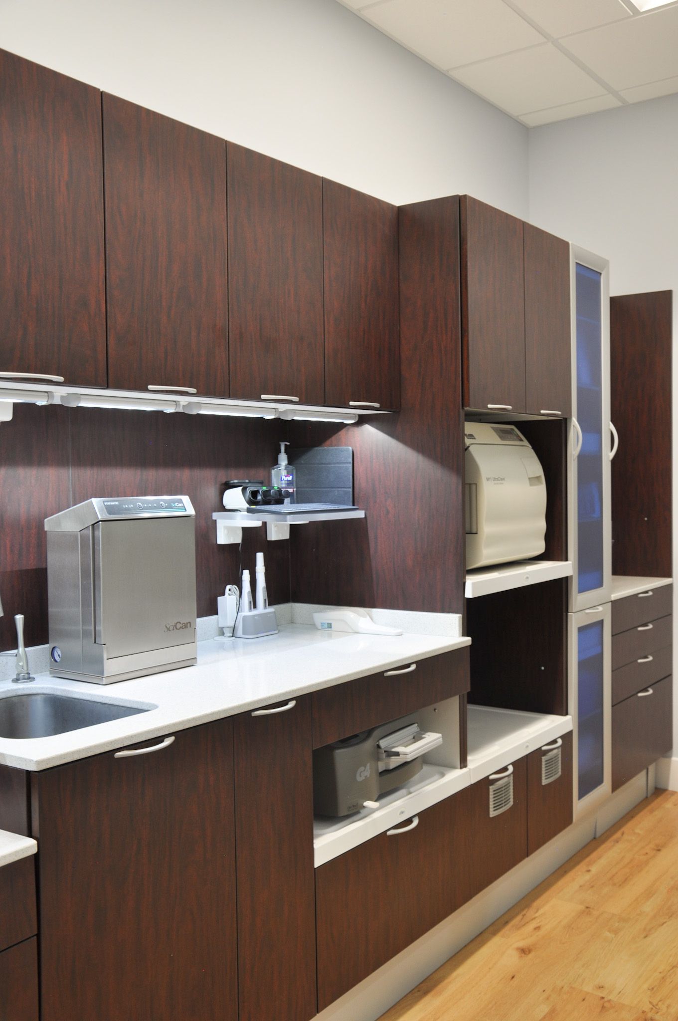 Dark wood dental office cabinets with sterilization equipment and sink.