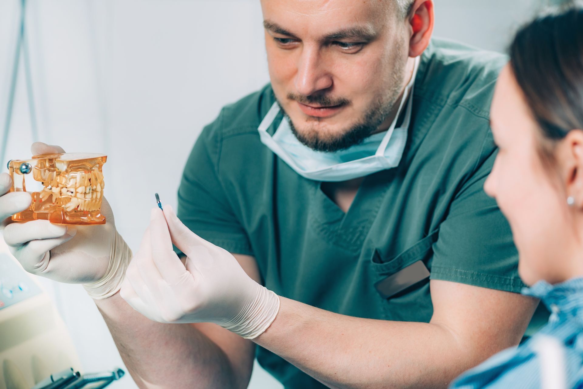 A dentist is holding a model of a tooth and talking to a patient.