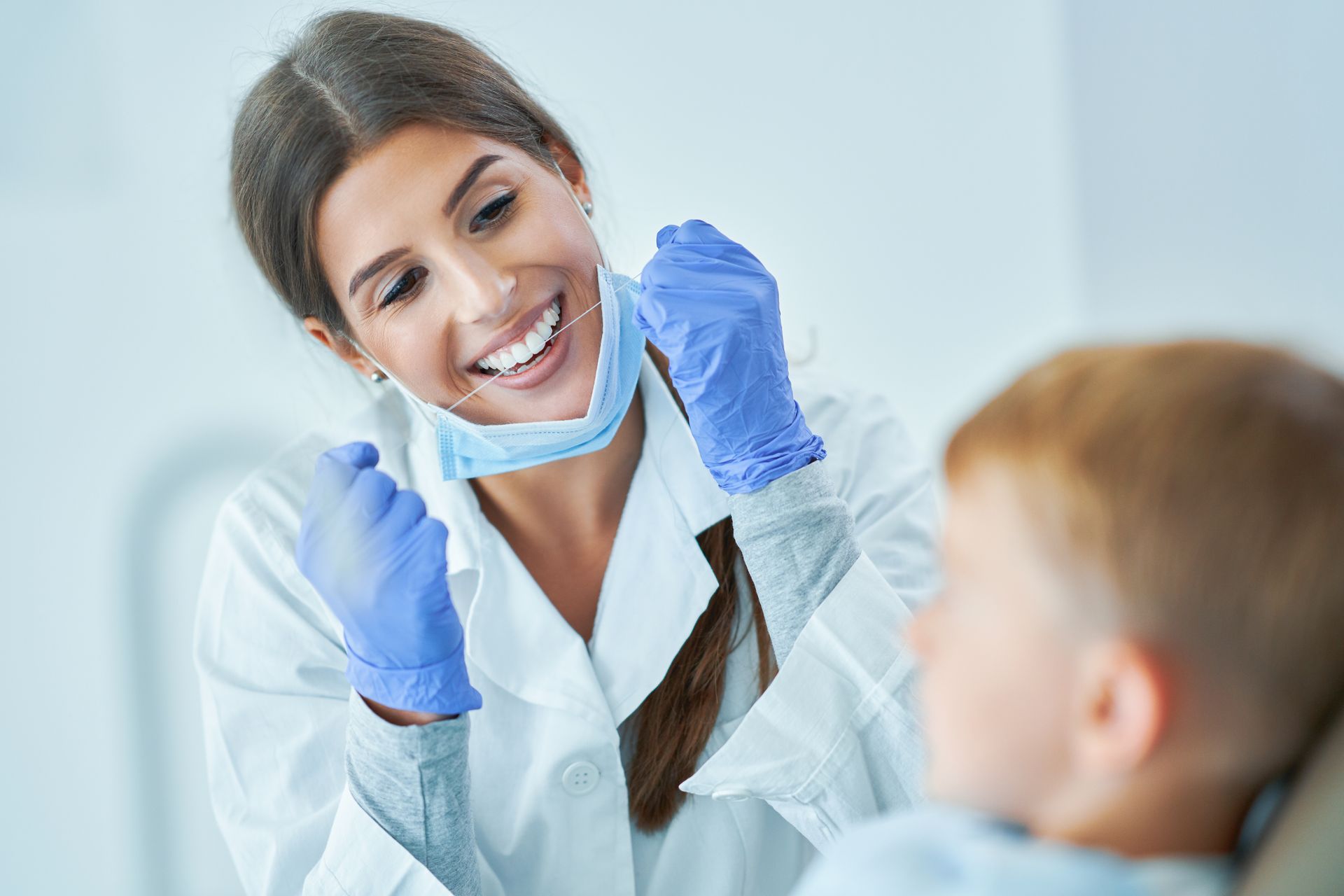 A female dentist is smiling while examining a young boy 's teeth.