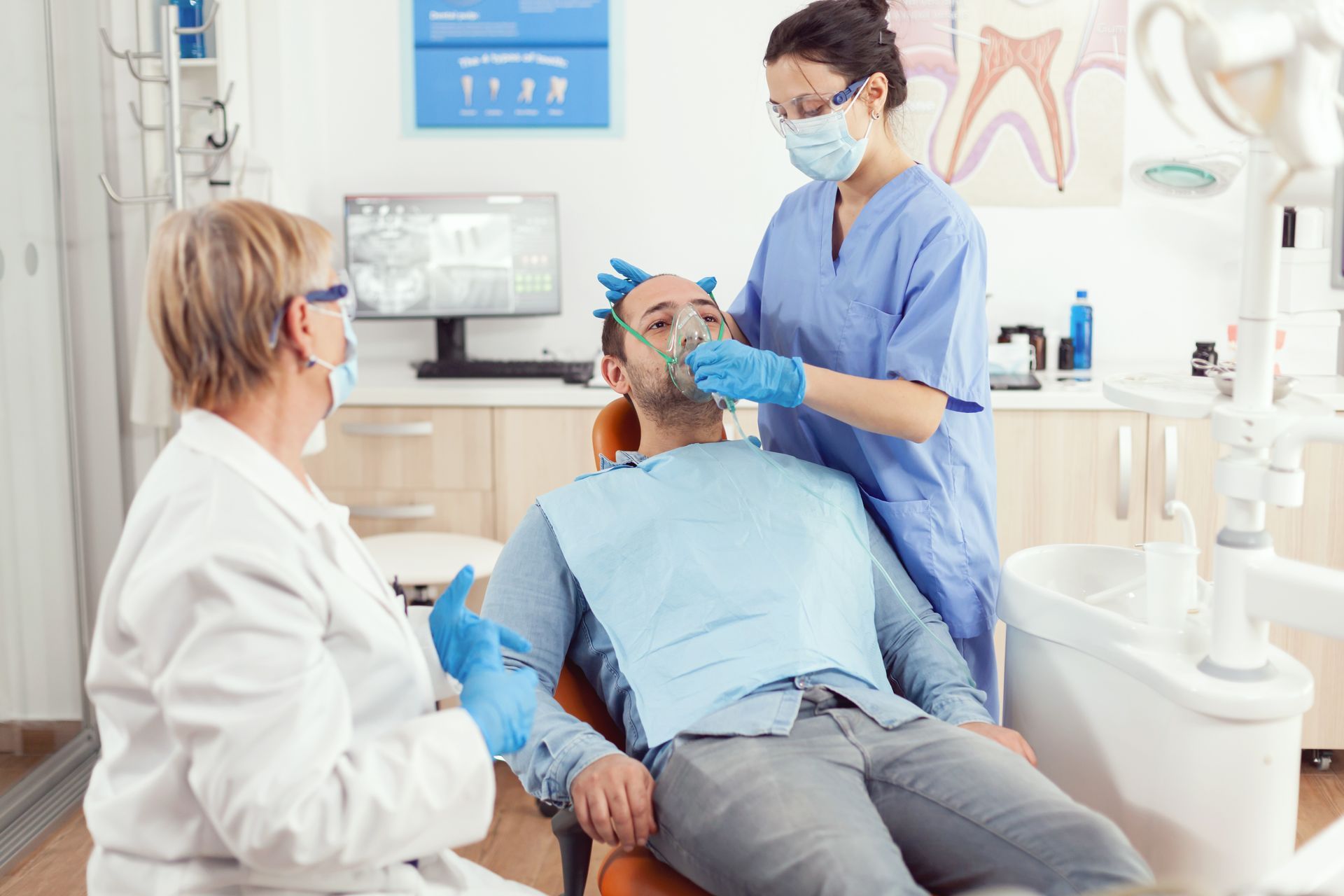 A man is sitting in a dental chair getting his teeth examined by two dentists.