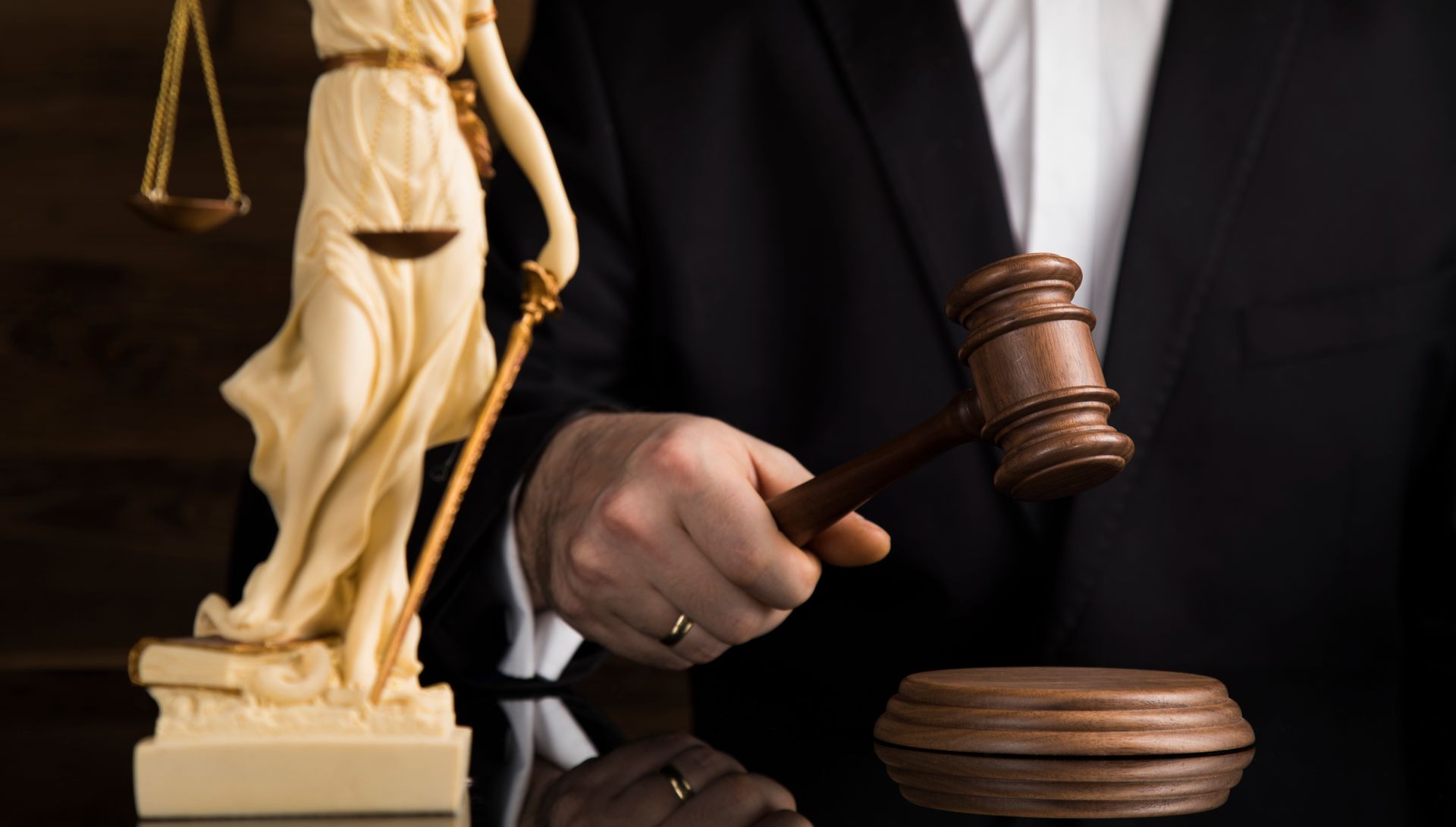 A person in a suit holding a gavel near a statue of Lady Justice.