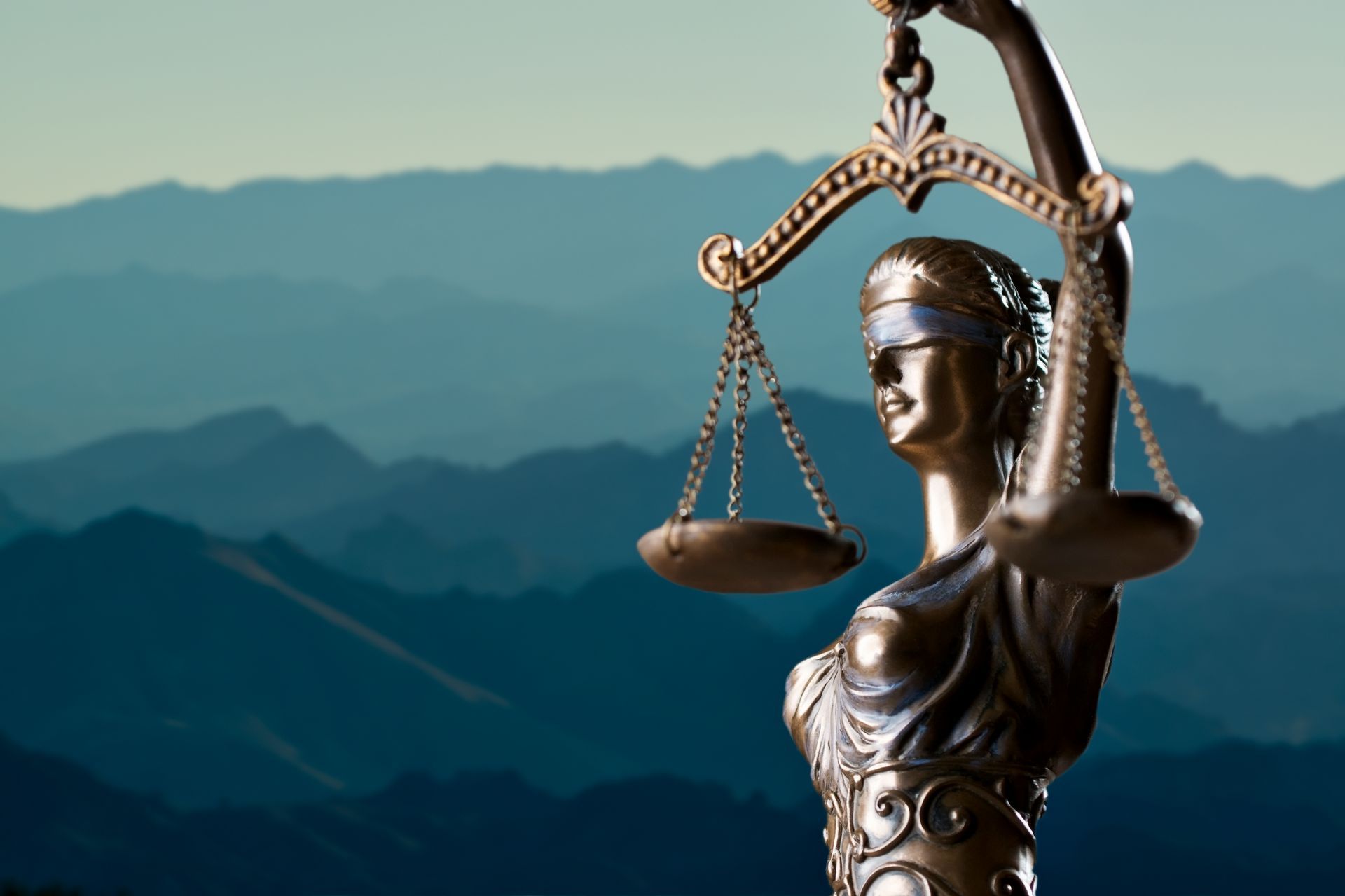 A statue of lady justice holding scales in front of mountains
