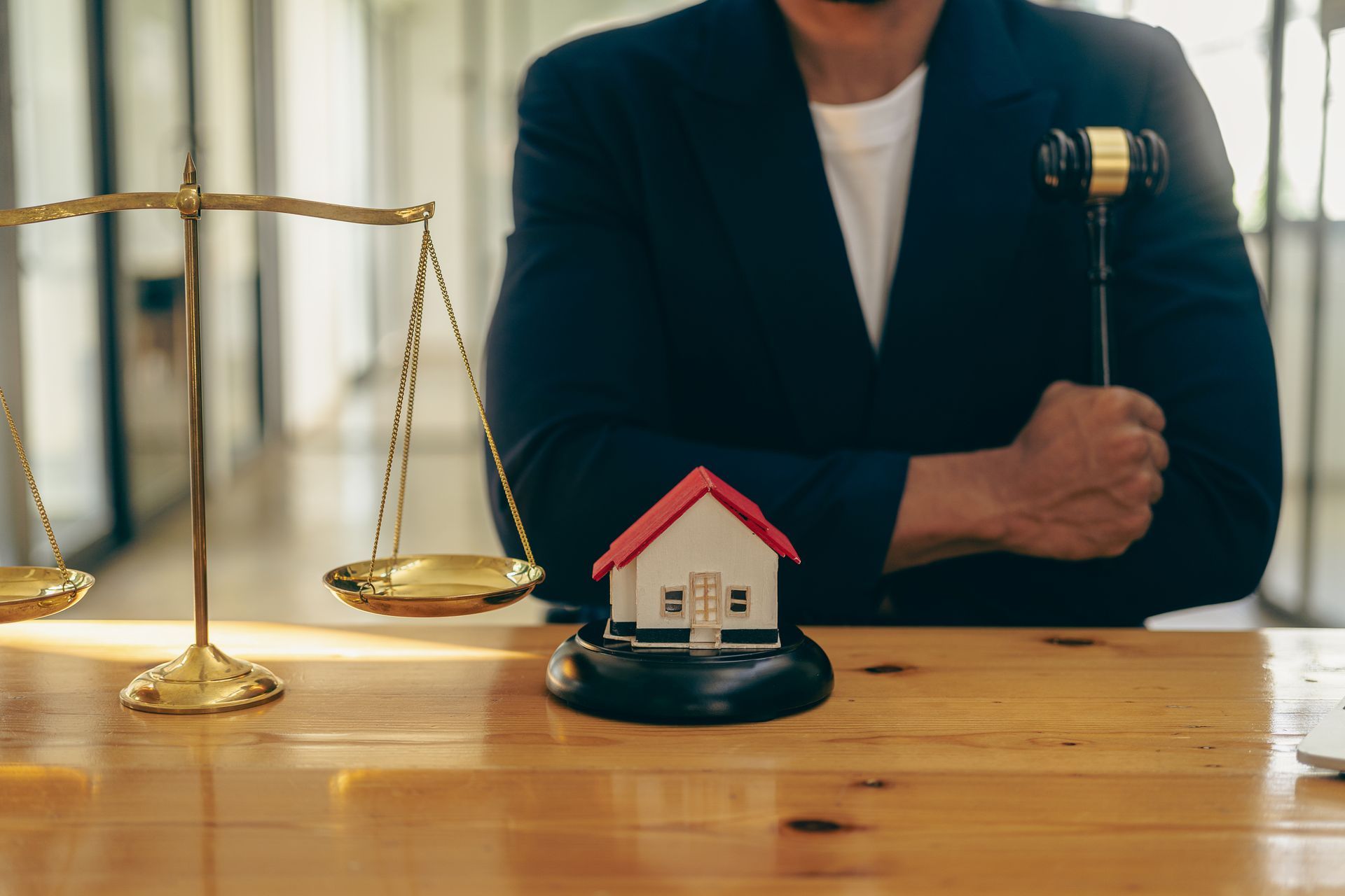 A man is holding a gavel in front of a scale and a model house.