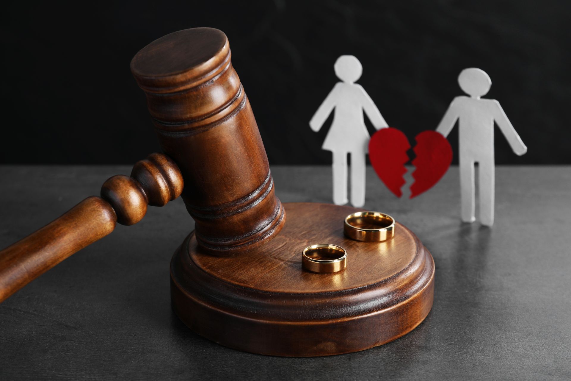 A wooden gavel, wedding rings, & paper figures with a broken heart, symbolizing a divorce attorney.