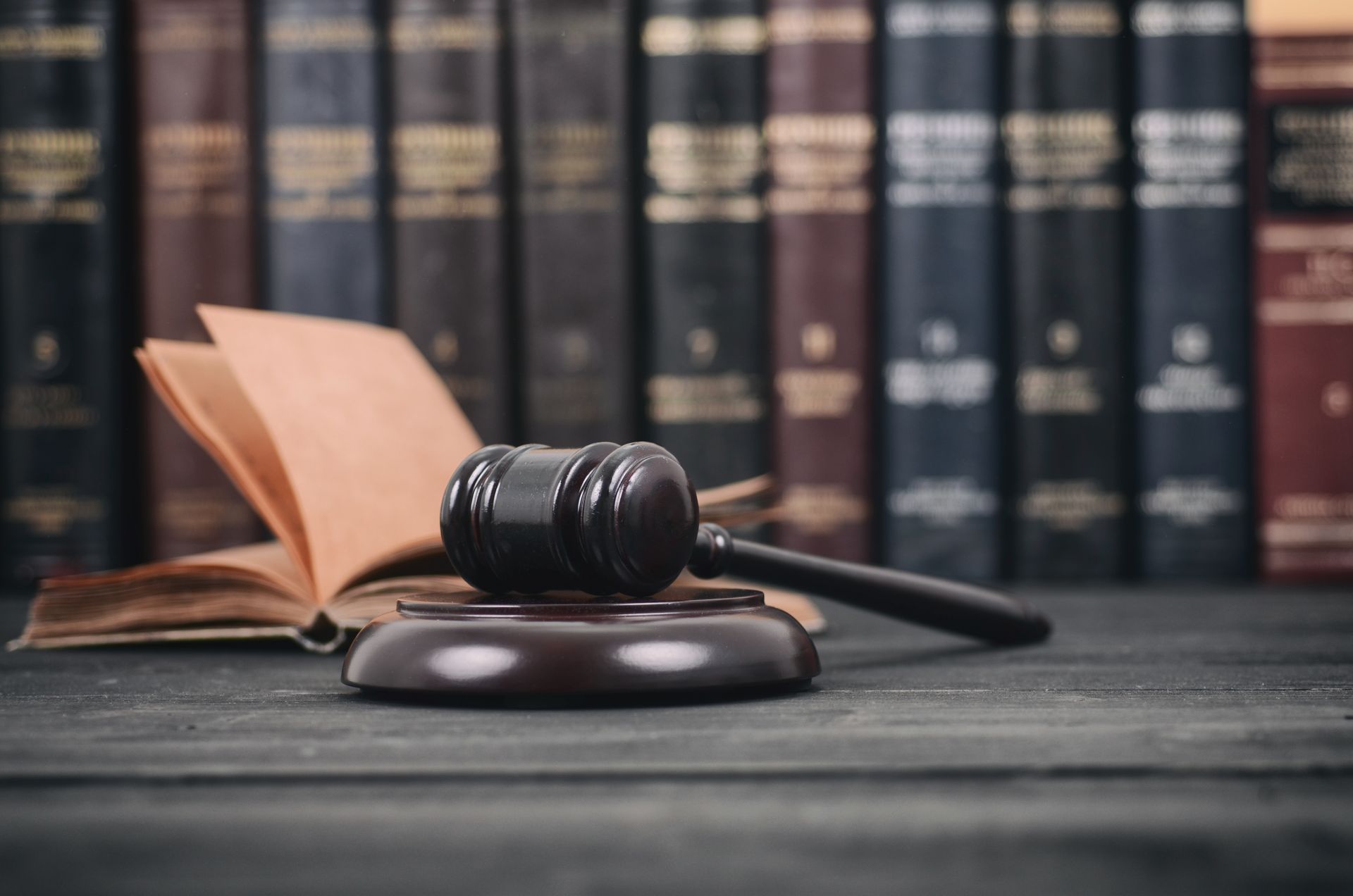 A wooden judge 's gavel is sitting on a wooden table in front of a row of books.