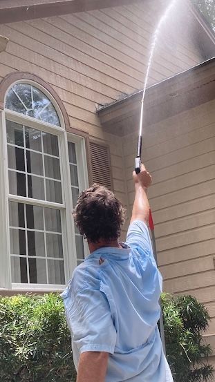 A man is cleaning the roof of a house with a hose.