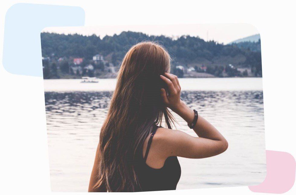 women dressed in black standing by the lake town and looking in the distance, holding hand in her hair