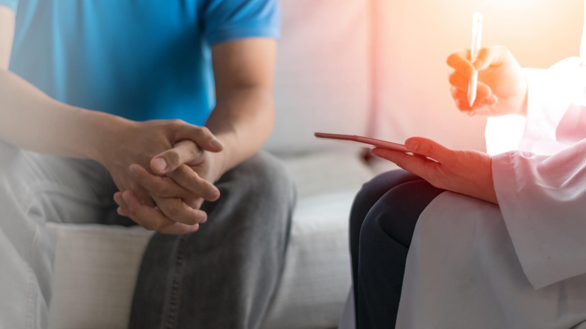 ivf specialist in a white coat and a male patient in a blue t-shirt sit together, the doctor writing on his tablet