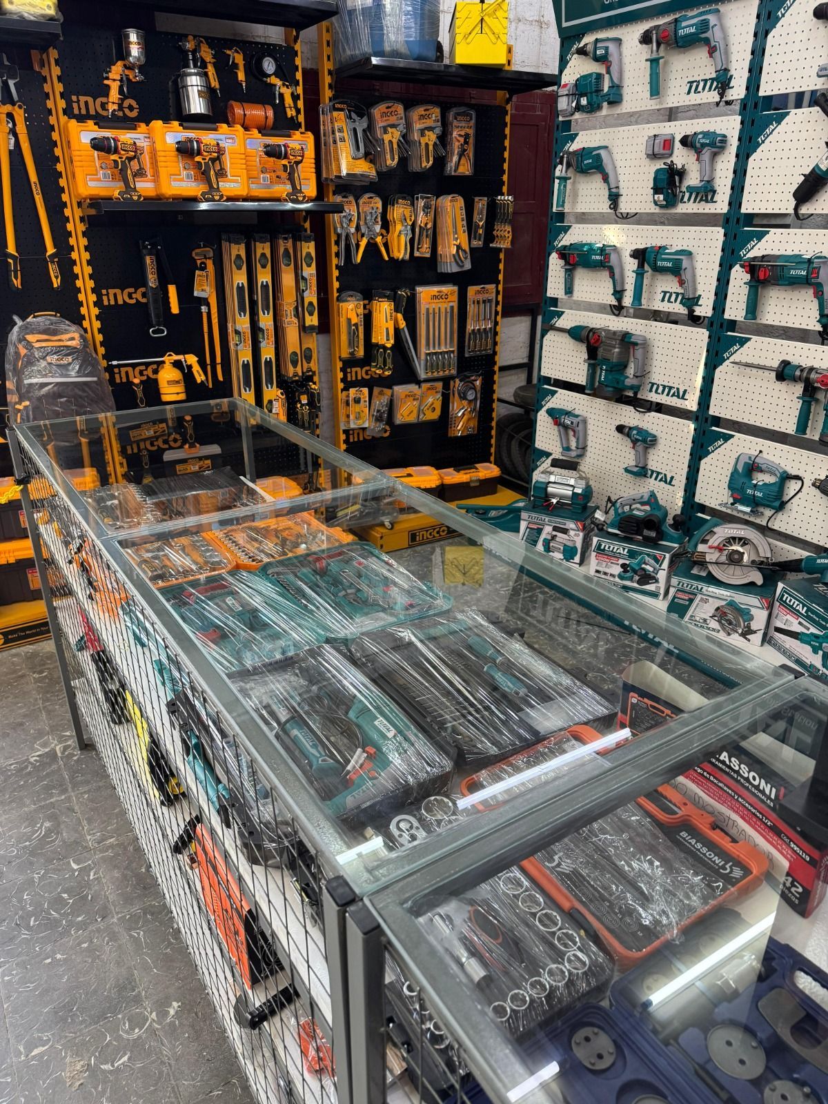 Exhibición de tienda de herramientas con diversas herramientas eléctricas, juegos de herramientas y accesorios en estantes y en un mostrador de vidrio.