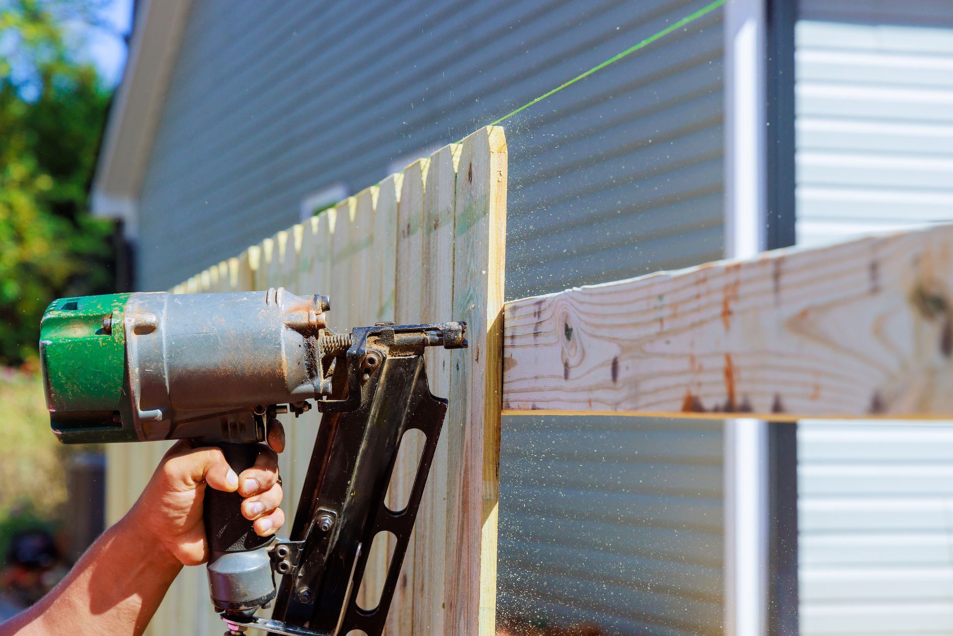 A person using a nail gun to attach wooden panels for a fence.