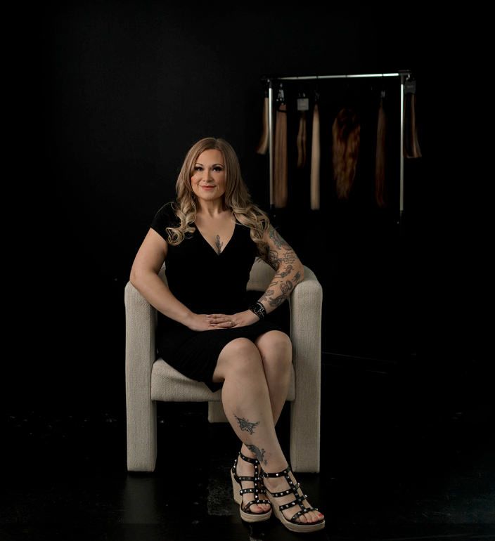 A woman is sitting in a chair in front of a rack of clothes.