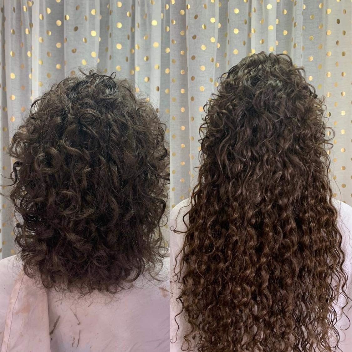 Two women with curly hair are standing next to each other in front of a curtain.
