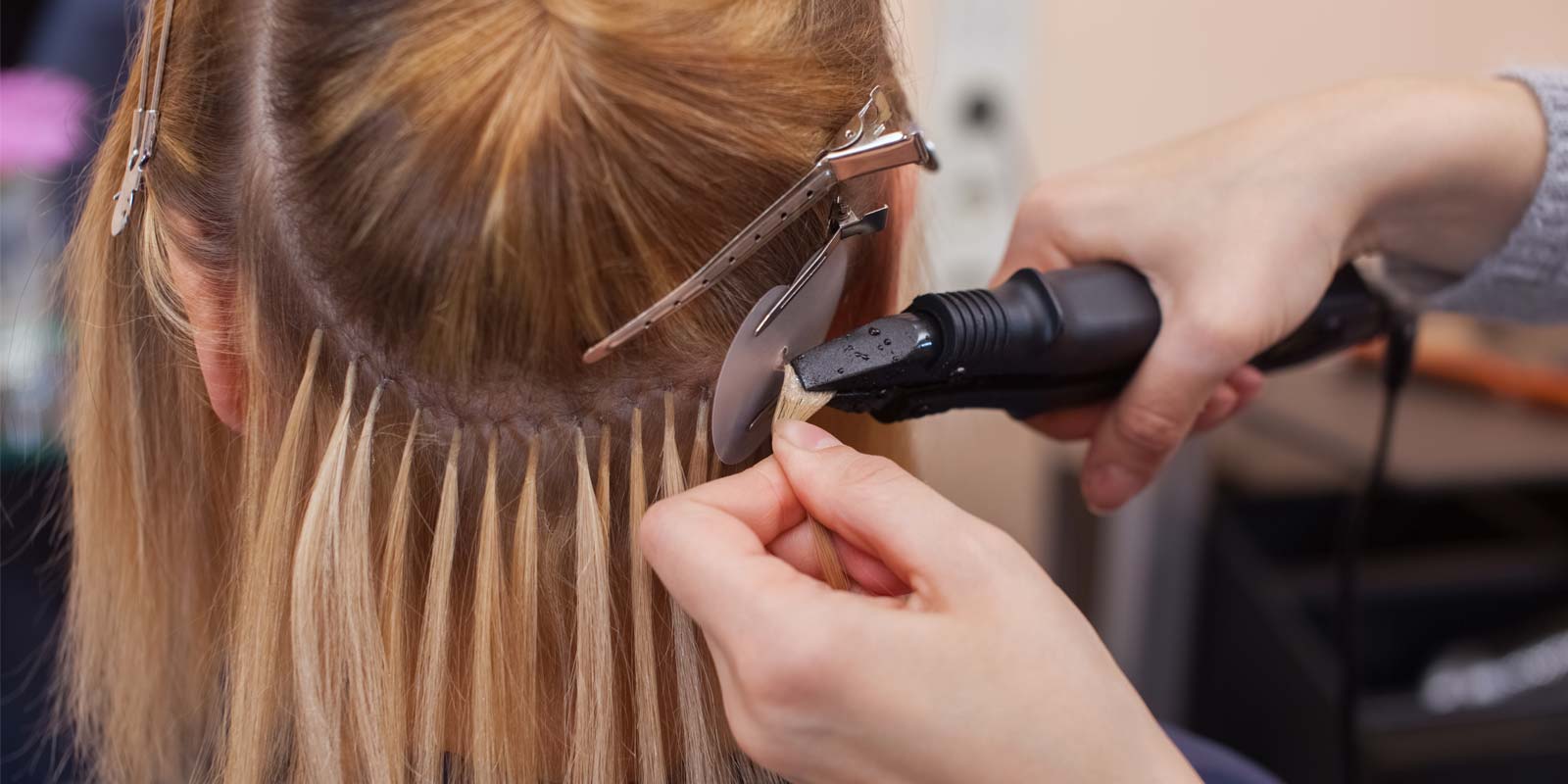 A woman is getting her hair extensions done by a hairdresser.