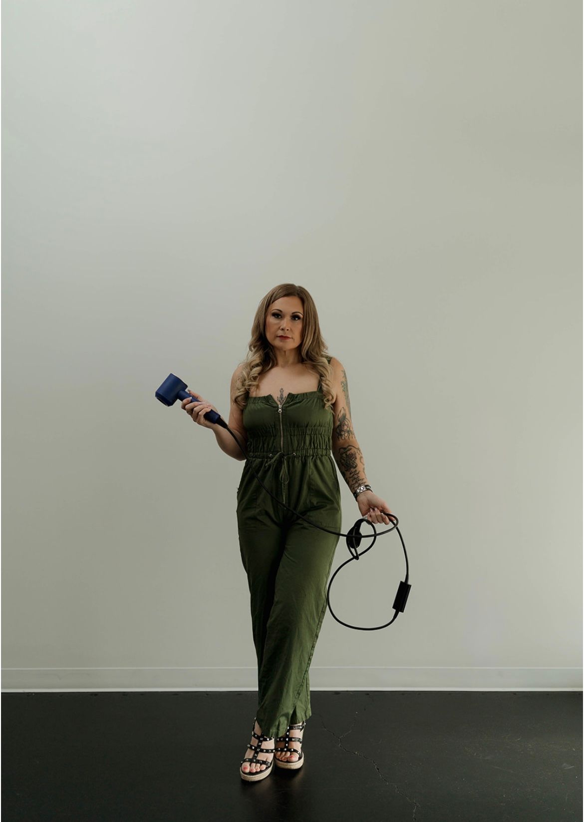 A woman in a green jumpsuit is holding a hair dryer and a cord.