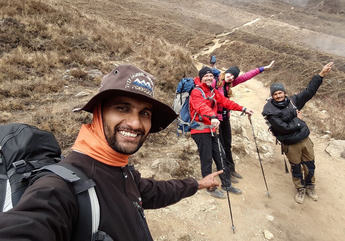 A trekking group smiling and pointing along a rugged Himalayan trail, enjoying their adventure together.