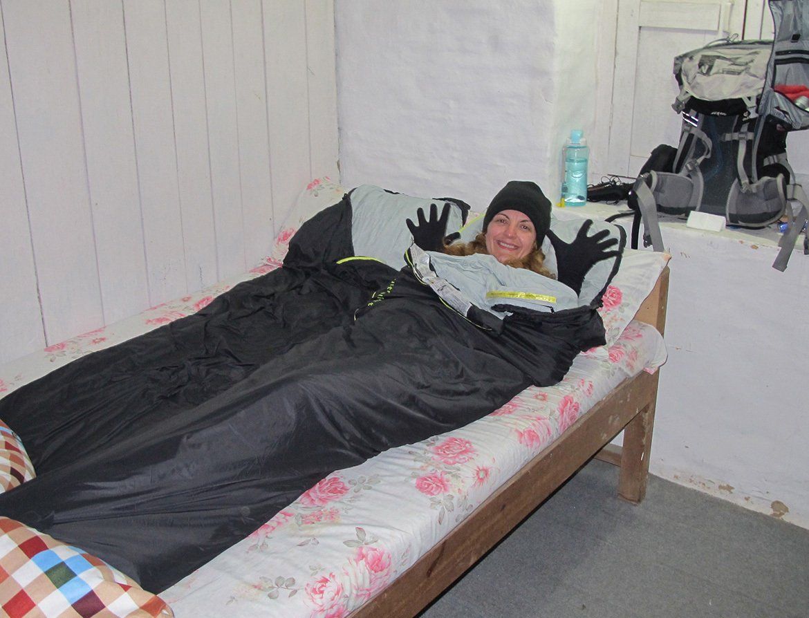 Trekker relaxing in a sleeping bag in a simple lodge bedroom, keeping warm after a day on the Annapurna Trek in Nepal.