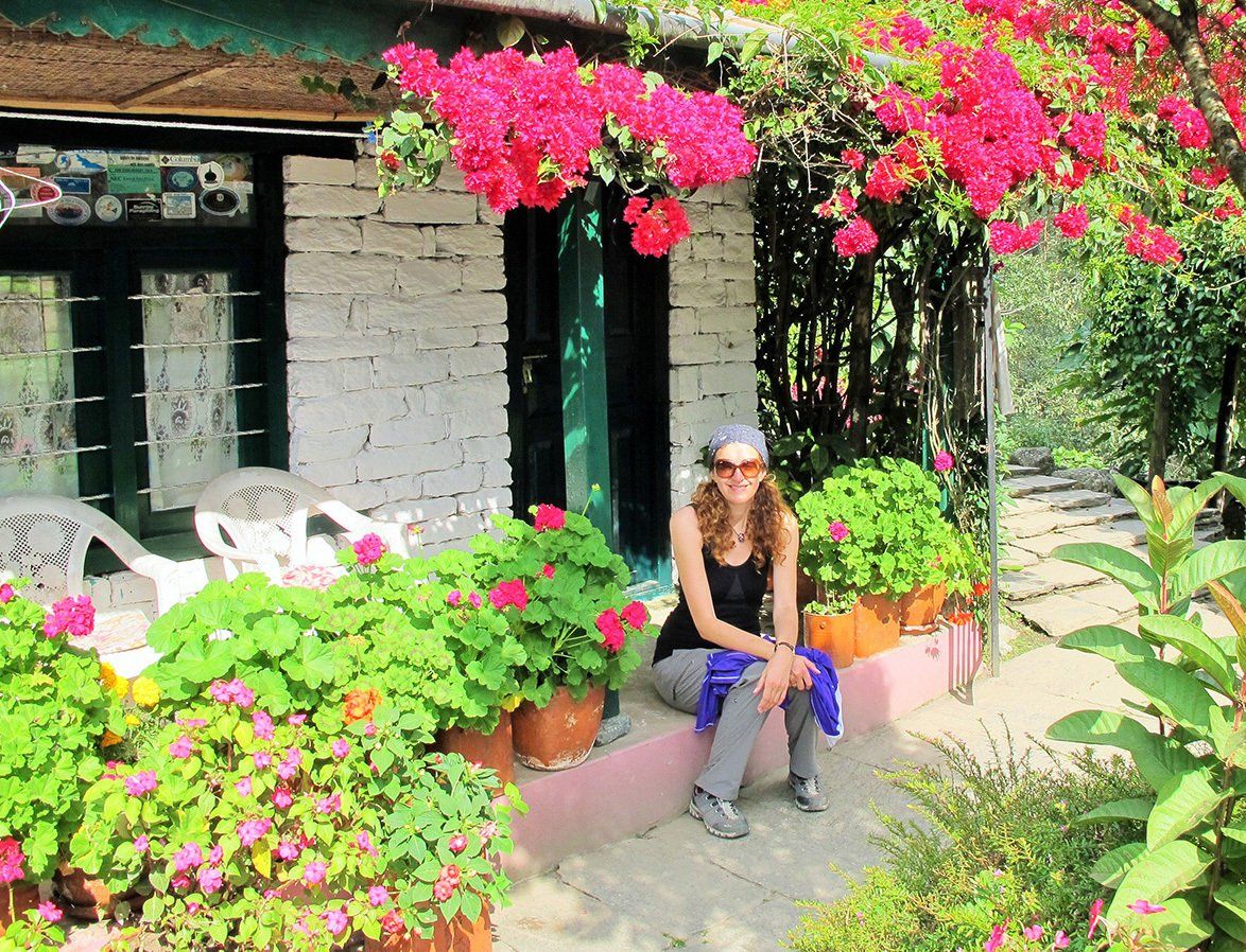 Female trekker relaxing on a flower-filled terrace at a charming guesthouse along the Annapurna Trek in Nepal.