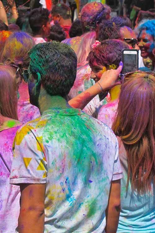 Colorful scene of people celebrating Holi in Pokhara, with vibrant powders covering their clothes and skin.
