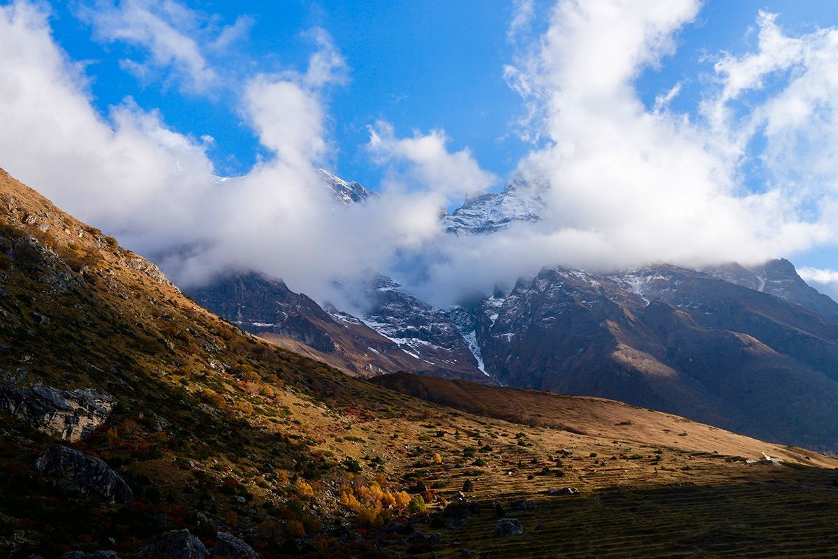 A breathtaking view of the Nar Phu mountains, partially covered by clouds, with golden autumn hues in the foreground.