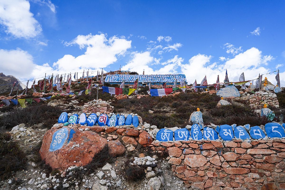 Colorful Tibetan prayer stones and prayer flags in the Nar Phu Valley, set against a deep blue sky and rugged terrain.
