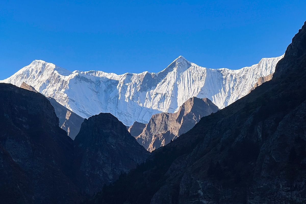Towering, snow-covered peaks of the Nar Phu region, standing against a clear blue sky with dramatic shadows.