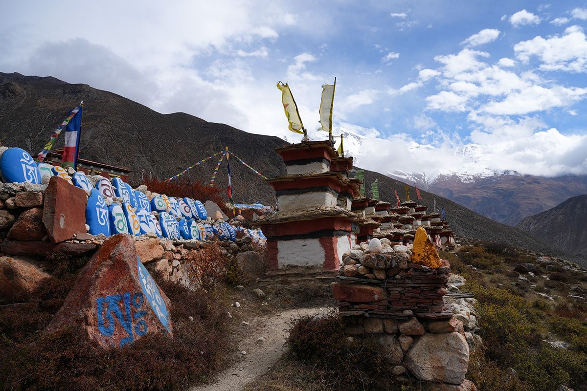Traditional Tibetan-style stupas and prayer stones with vibrant colors, set against the backdrop of snowy peaks.