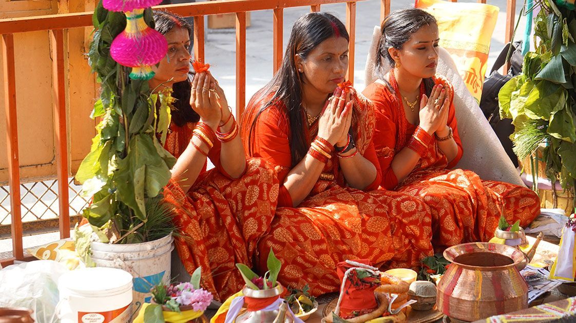 Three women in traditional red attire participate in a Nepali ceremony, with their hands in a prayer