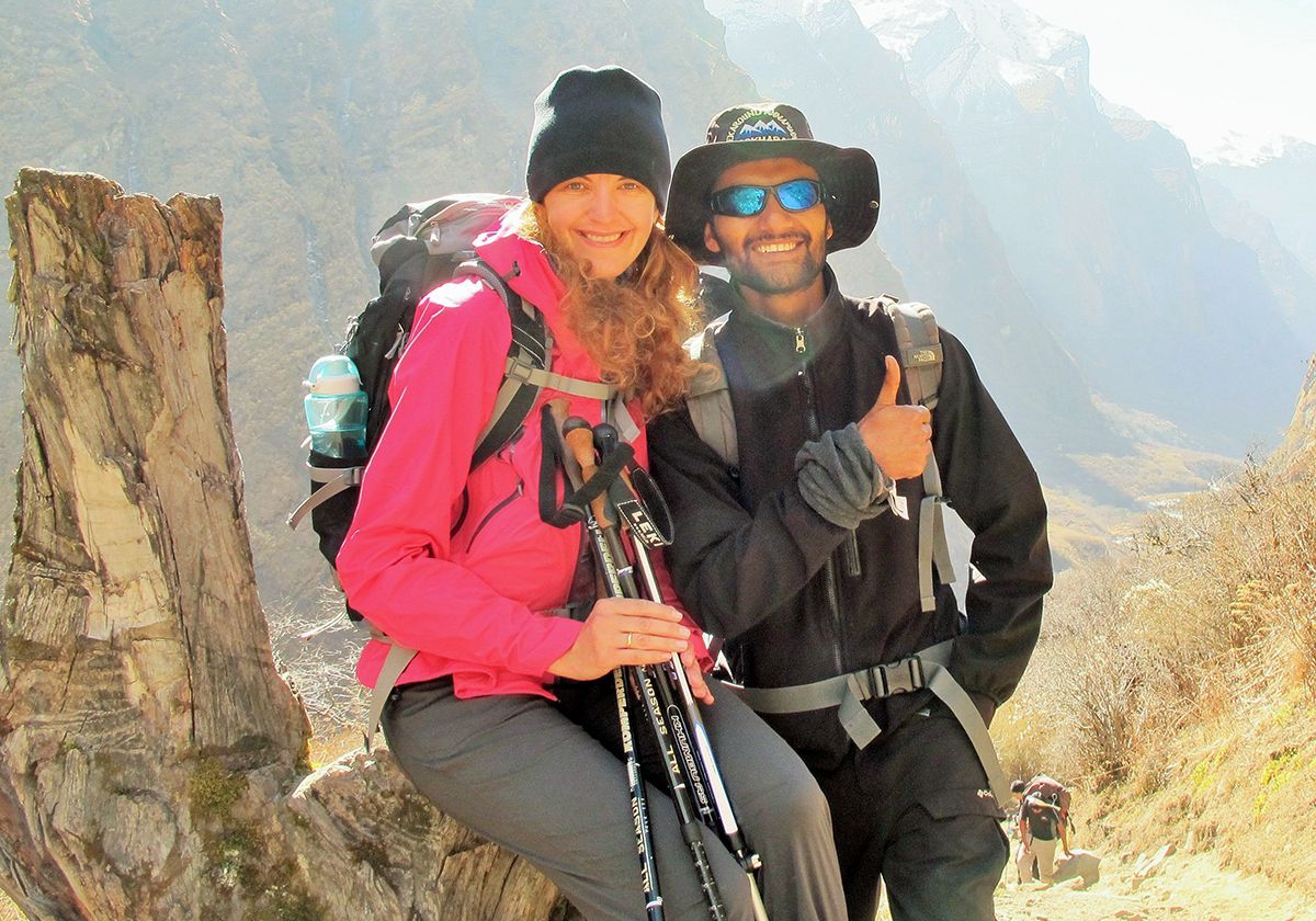 A female trekker in pink and her guide smiling in the Himalayas, sharing a moment of joy on the trail.