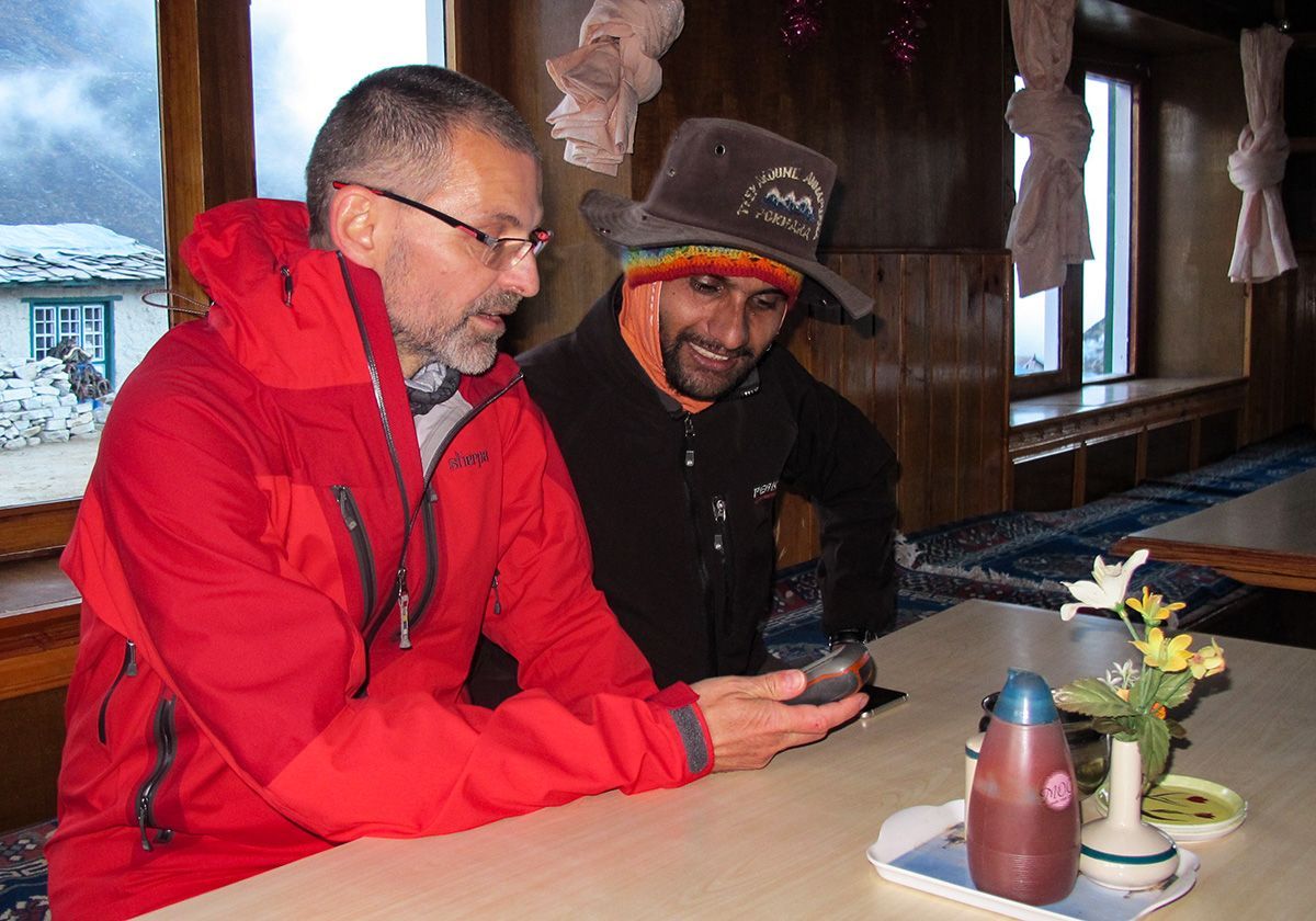Two trekkers in a cozy mountain lodge, smiling and looking at a device after a long day of hiking.
