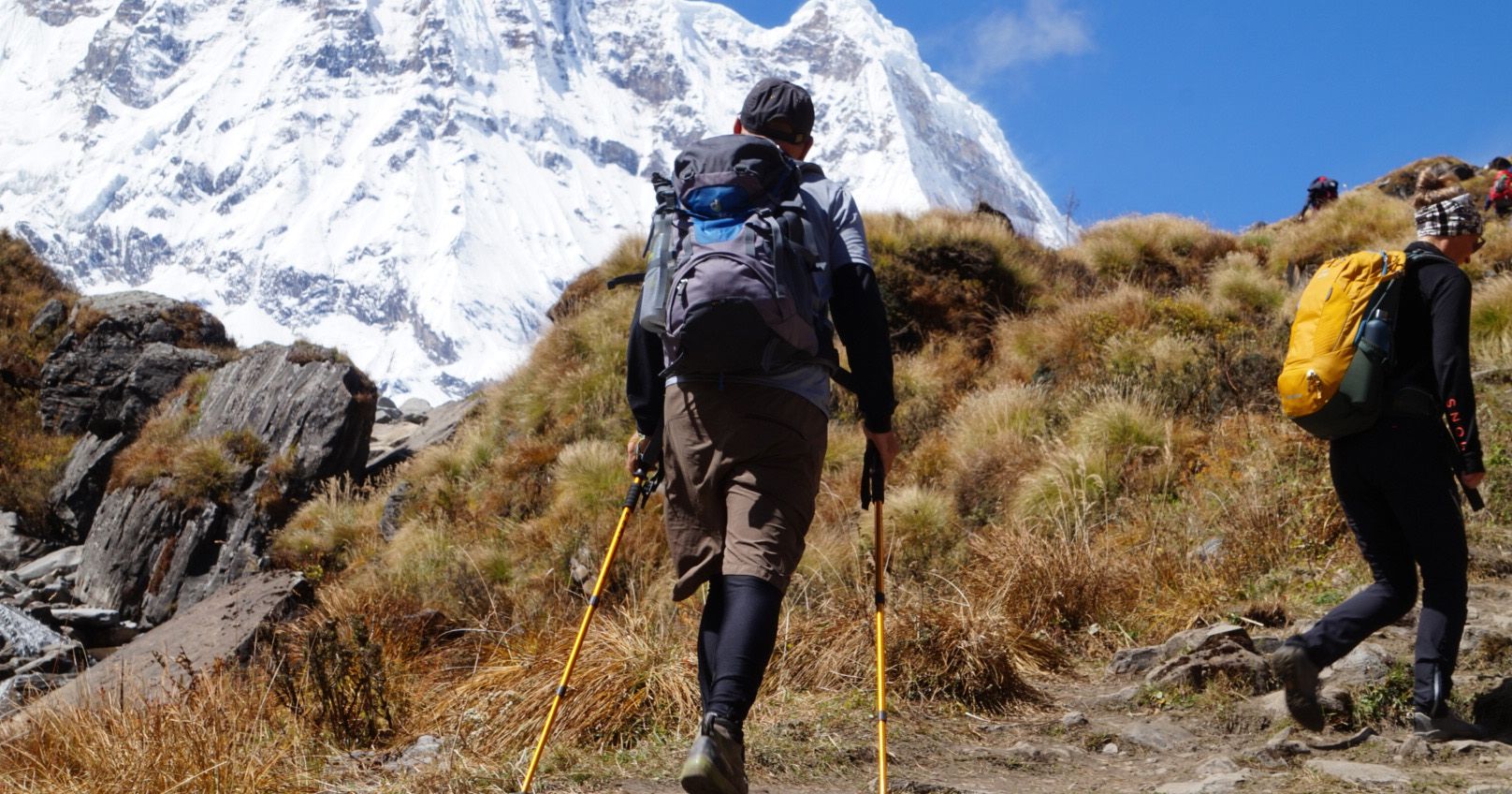 Trekkers hiking in the Annapurna region of Nepal, carrying backpacks and using trekking poles.