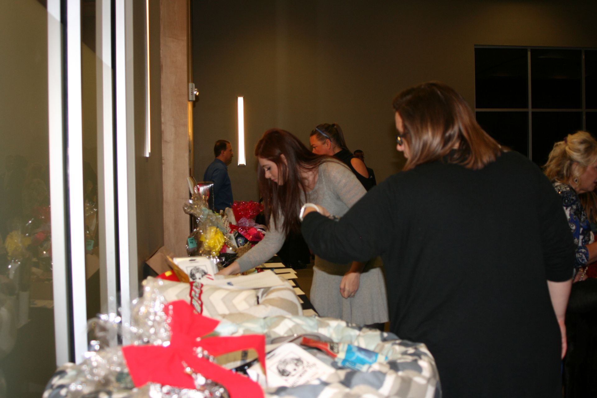 People gather around a table covered in items and fabric, browsing offerings at an indoor event.