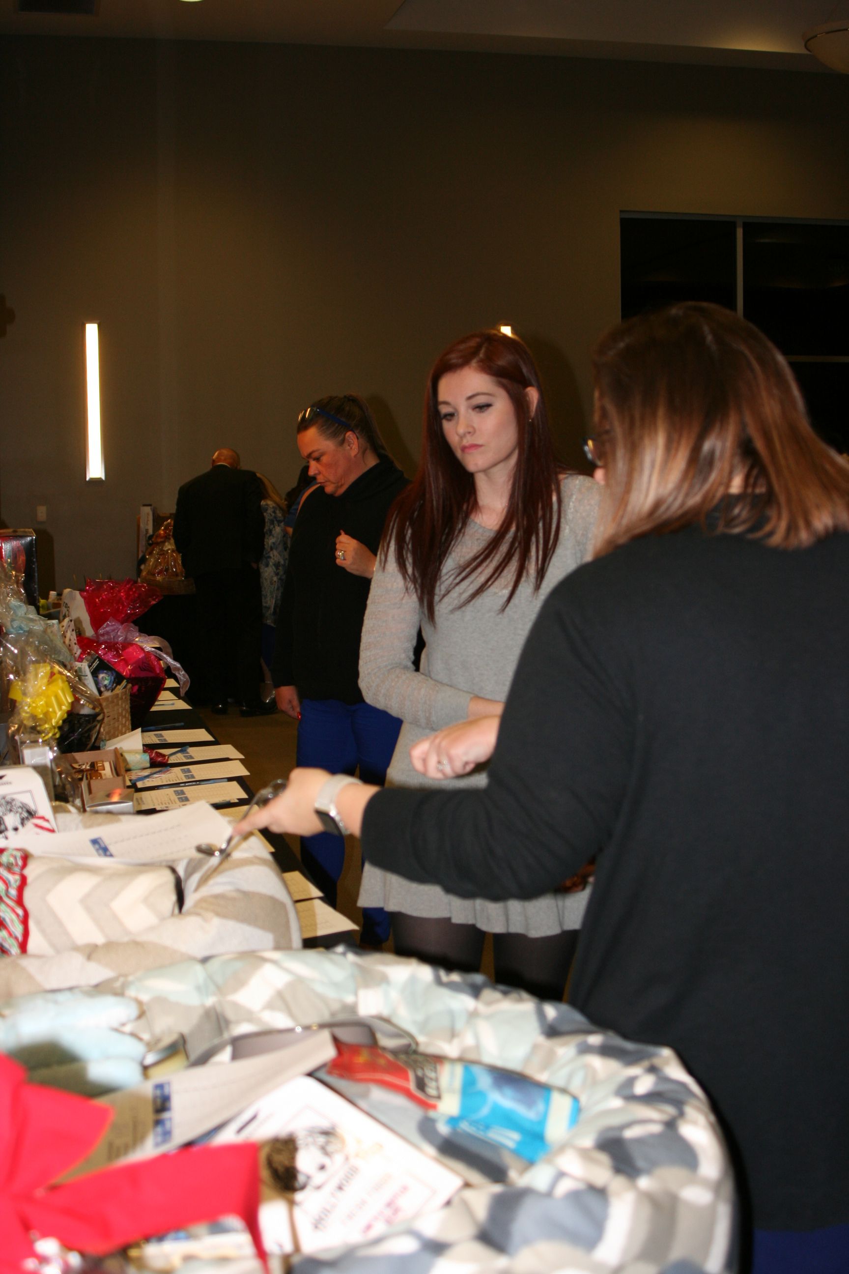 Two people in an indoor room stand at a table filled with various items, looking down and interacting with them.