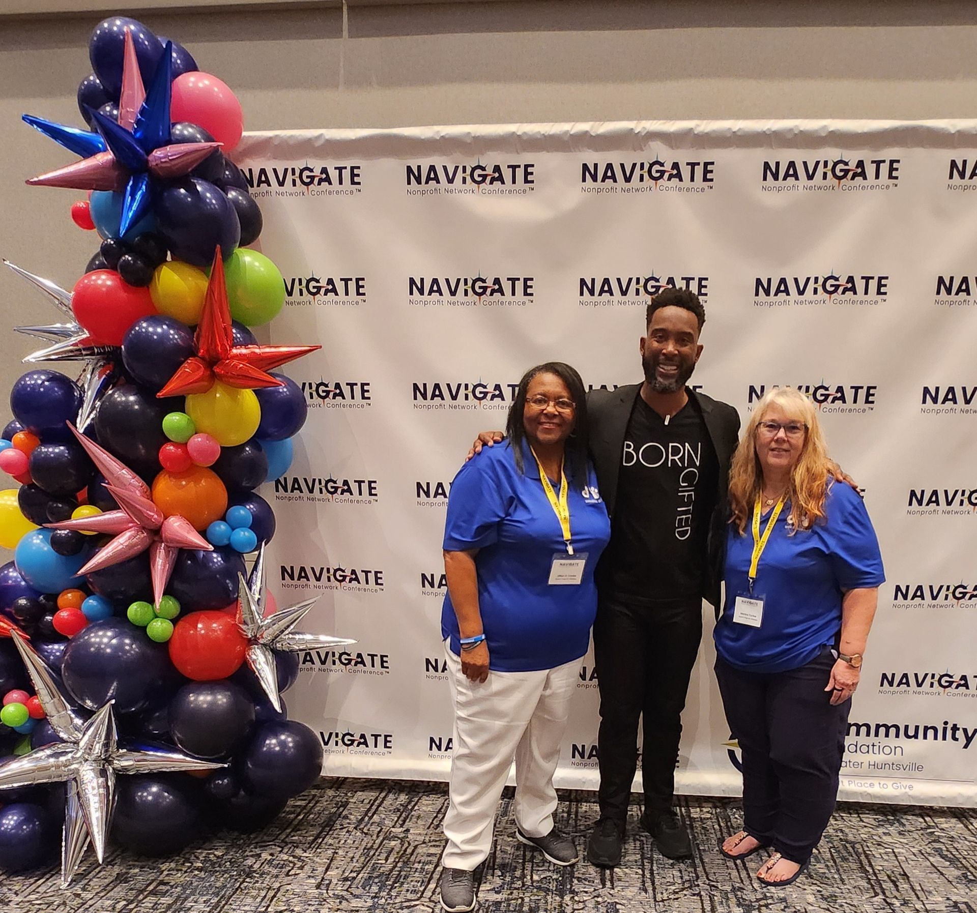 Three people pose in front of a Navigate backdrop next to a balloon decoration with stars at an indoor event.