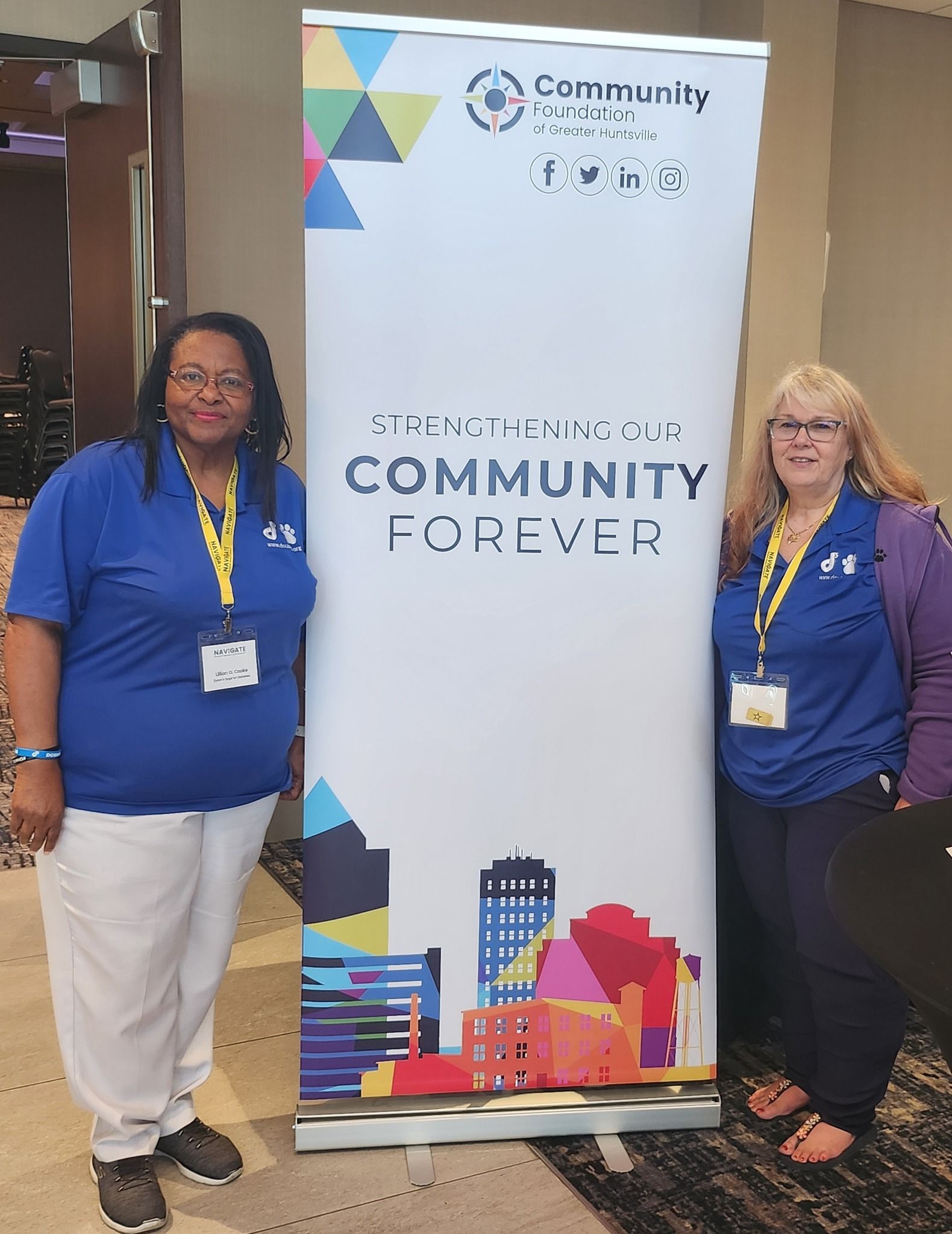 Two people in blue polo shirts and lanyards stand beside a tall 