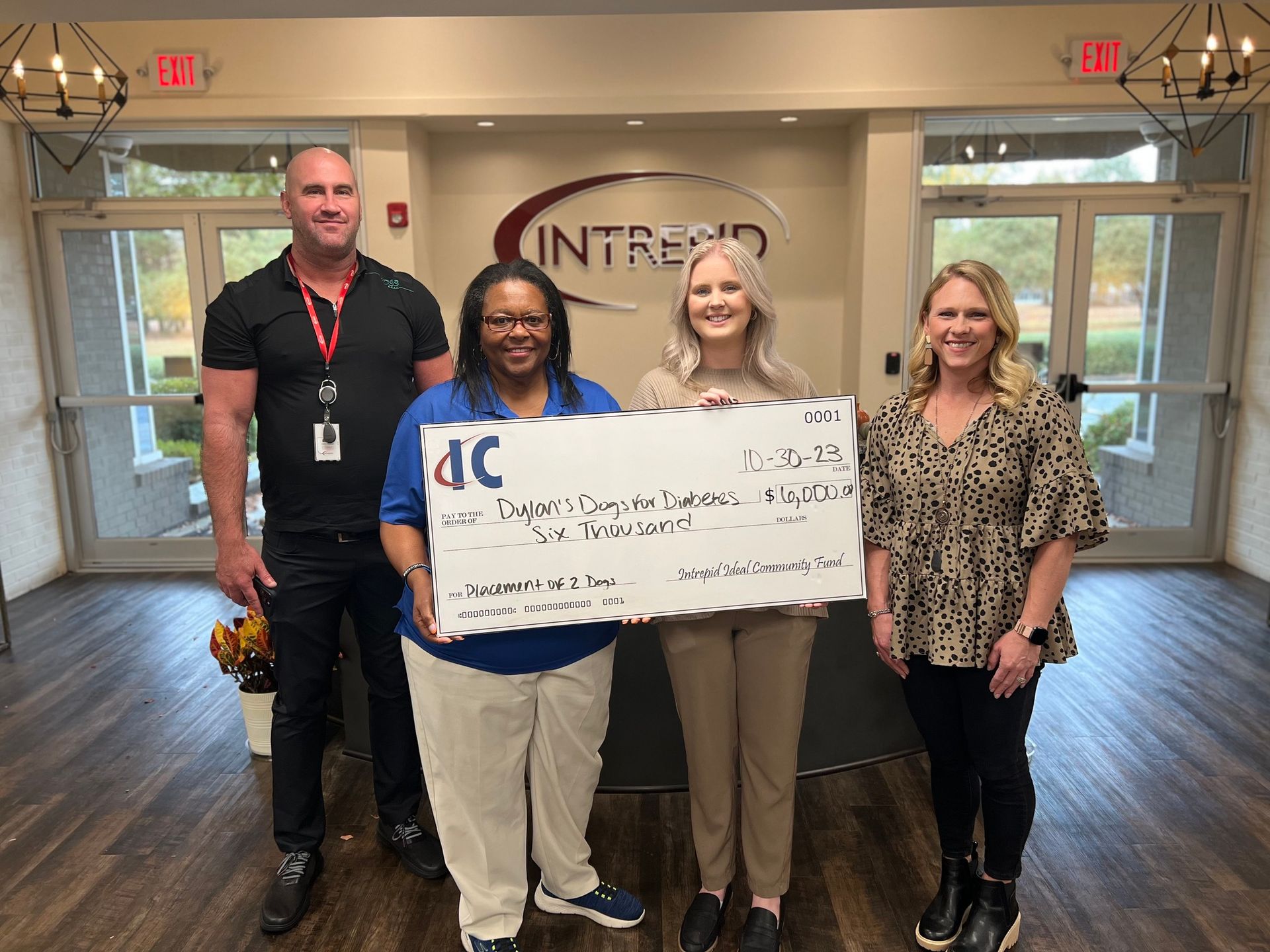 Four people standing in an office lobby hold a large ceremonial check featuring the Intrend logo.