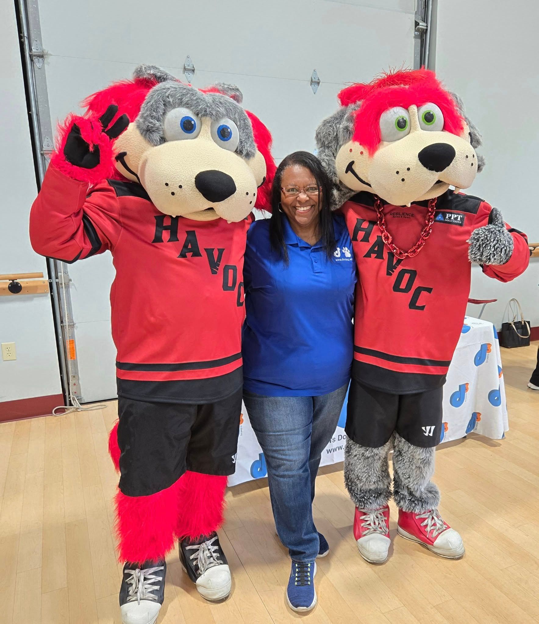 A person in a blue shirt stands between two mascots in red 