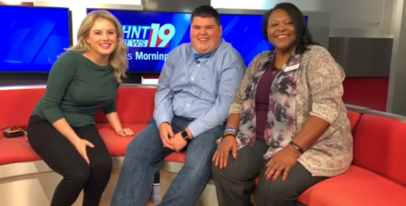 Three people sit on a red couch in a news studio with WHNT News 19 branding on the screens in the background.