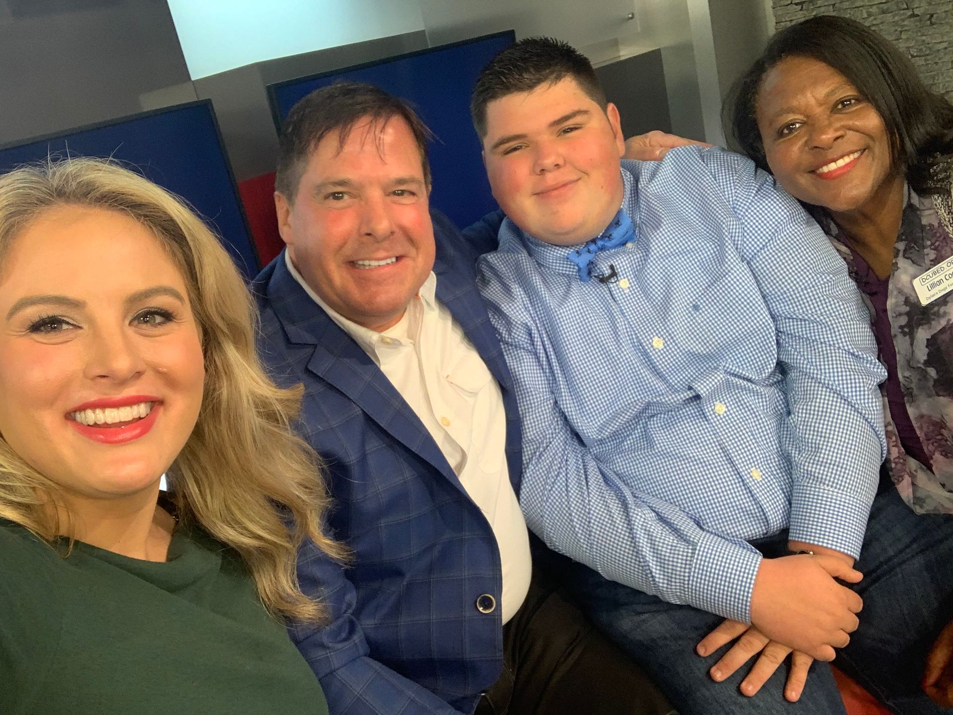 Four people smiling together for a group selfie in a professional studio setting.