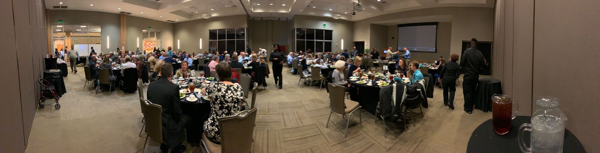 A panoramic view of an indoor conference or banquet hall with people seated at round tables for a meeting or event.