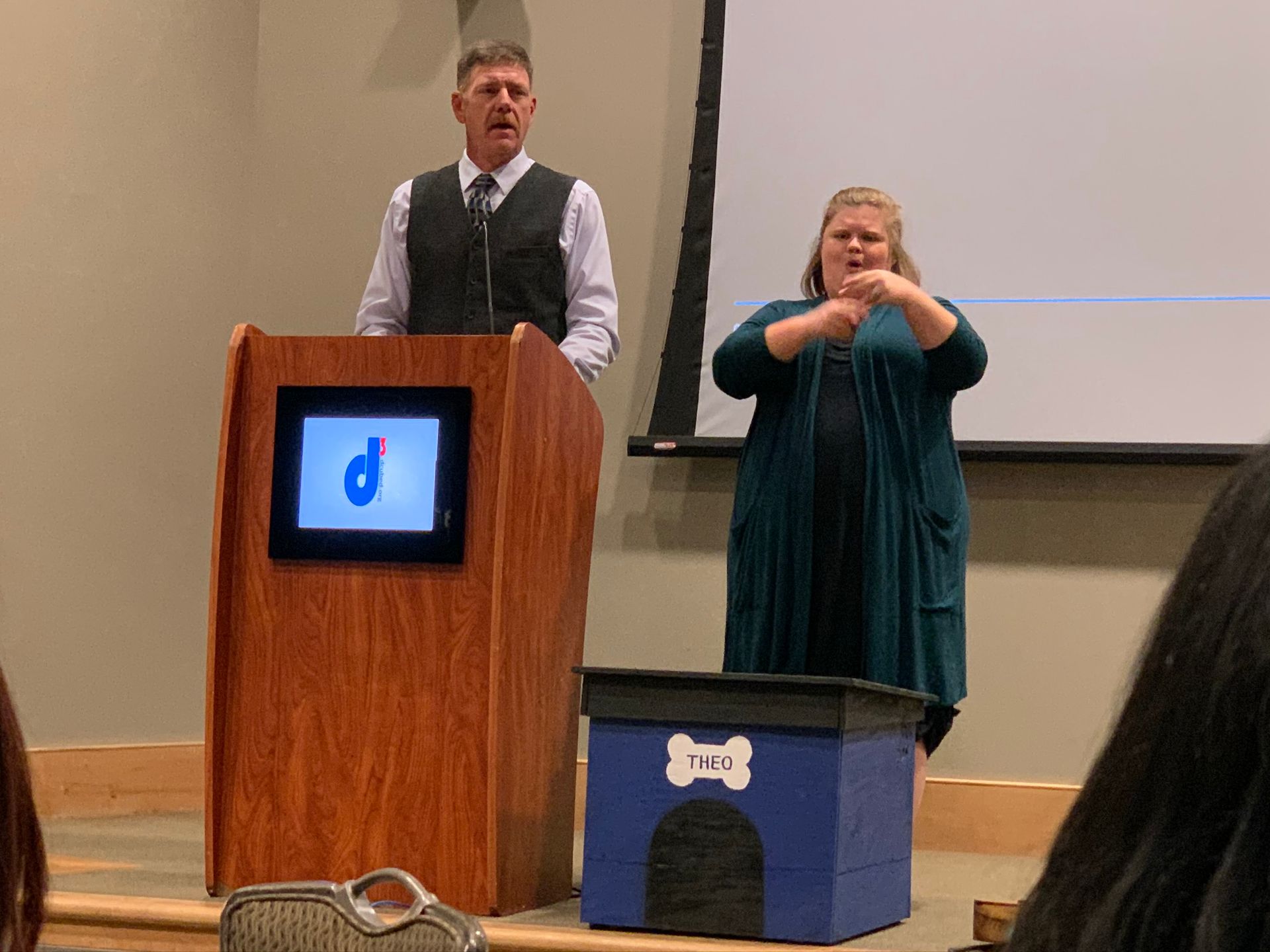 A speaker stands at a wooden podium with a 