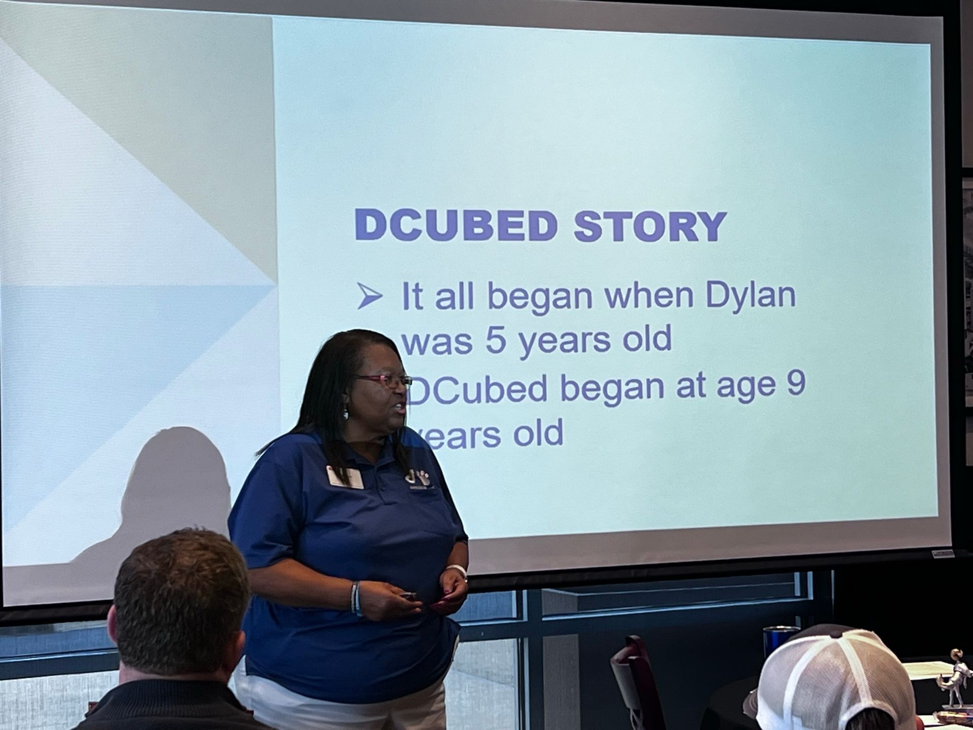 A speaker stands before a projector screen titled 