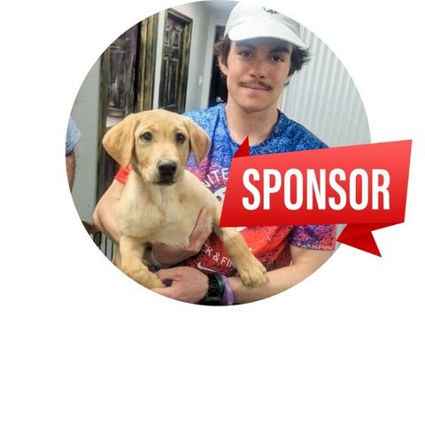 A person wearing a white hat holds a light-brown puppy. A red 