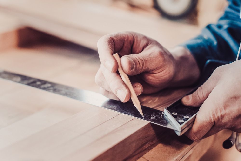Person Using a Pencil and Square to Measure and Mark Wood in a Workshop — Kalora Carpentry & Restorations in Charlestown, NSW