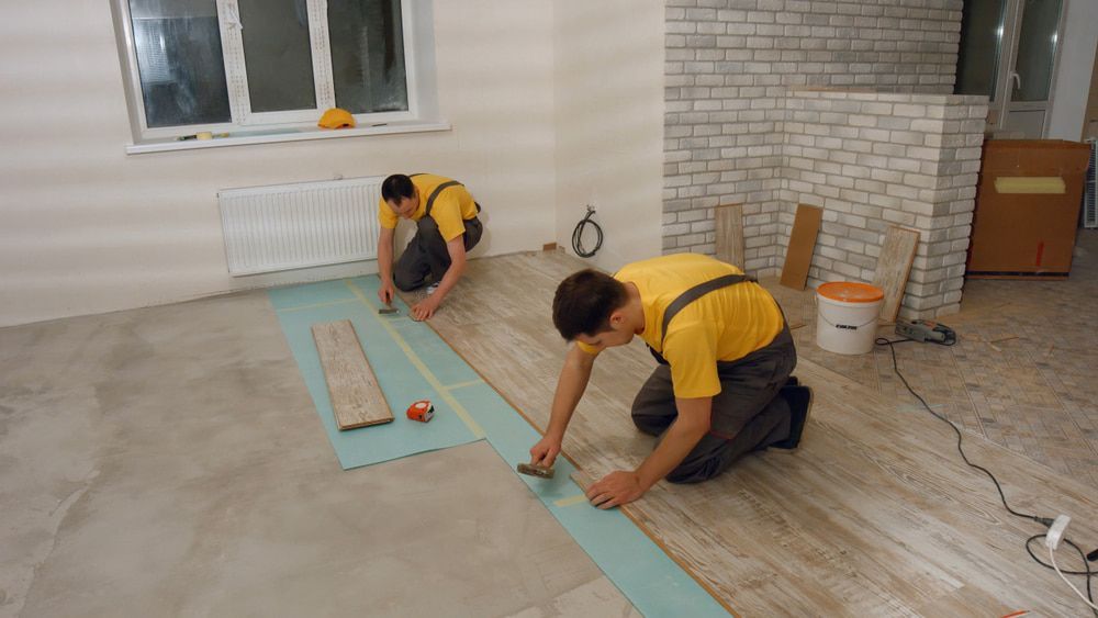 Two Workers Installing Wood Flooring in a Room — Kalora Carpentry & Restorations in Lake Macquarie, NSW