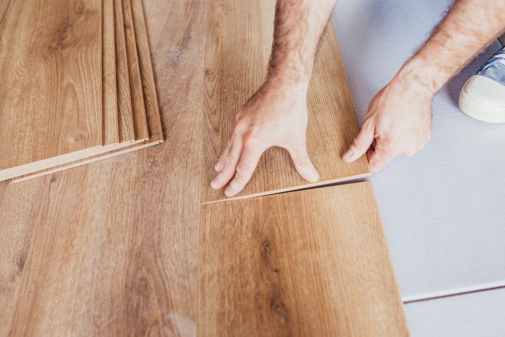 Person Installing Wooden Flooring; Hands Fitting a Plank — Kalora Carpentry & Restorations in Merewether, NSW