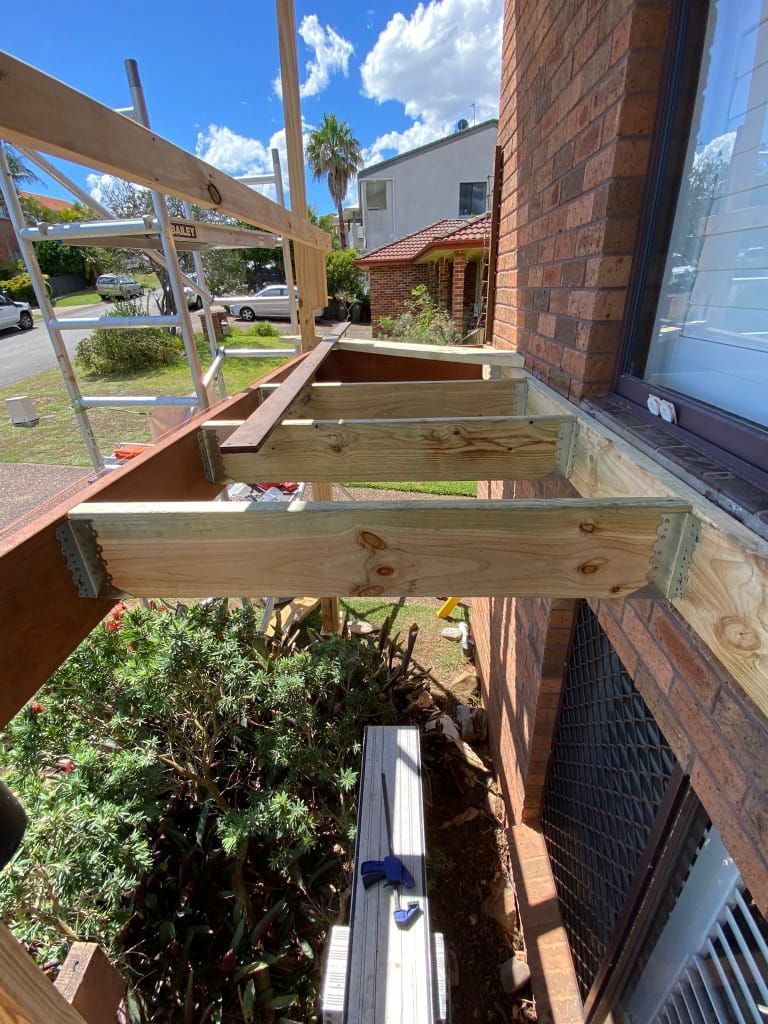A Wooden Deck Under Construction Next to a Brick Building — Kalora Carpentry & Restorations in Lake Macquarie, NSW