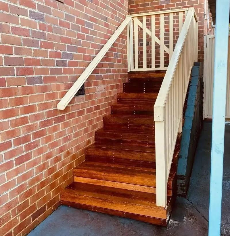 Wooden Outdoor Stairs With Tan Railings Against a Brick Wall — Kalora Carpentry & Restorations in Charlestown, NSW