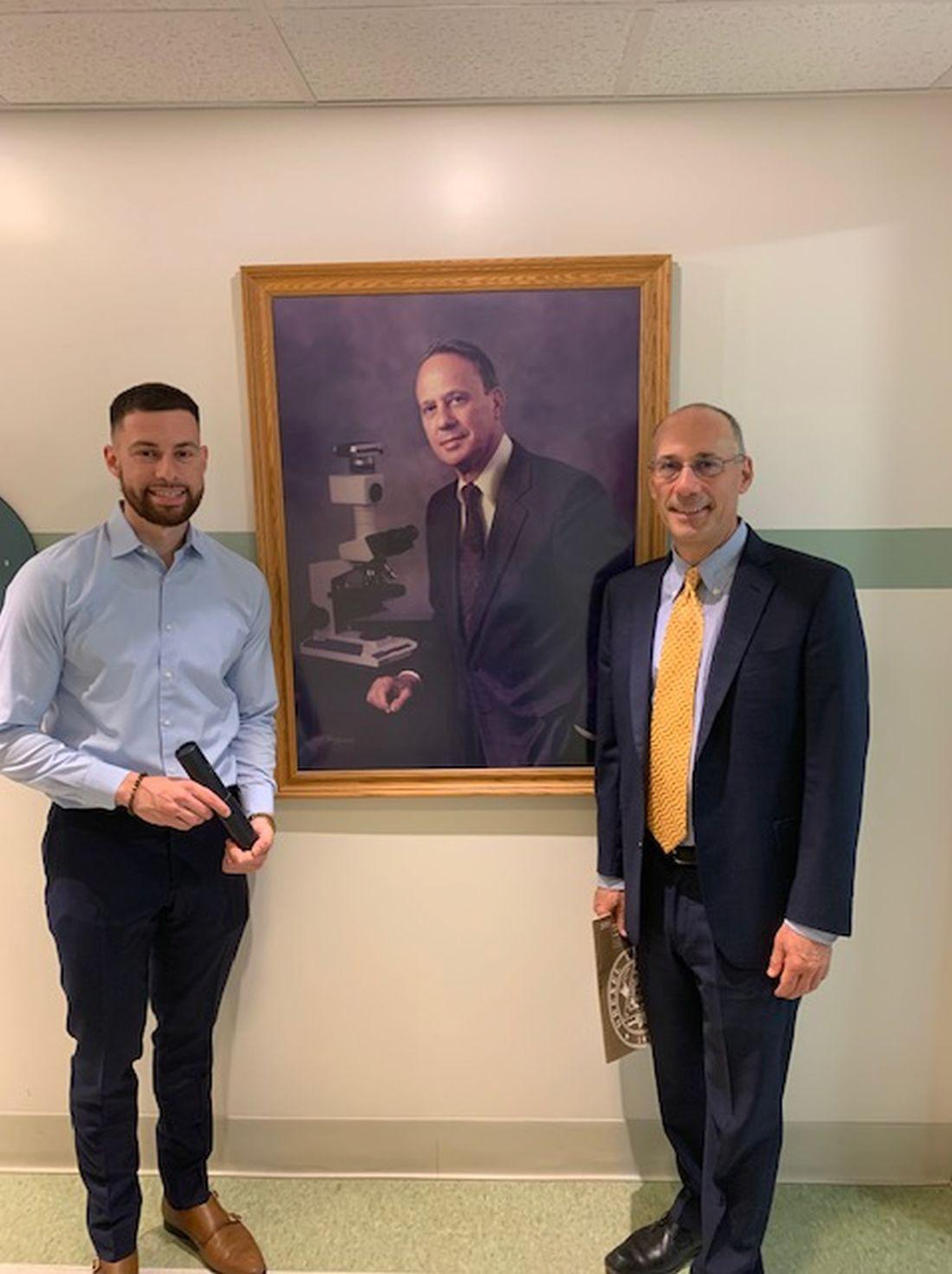 Two men in suits are standing in front of a painting of two men.