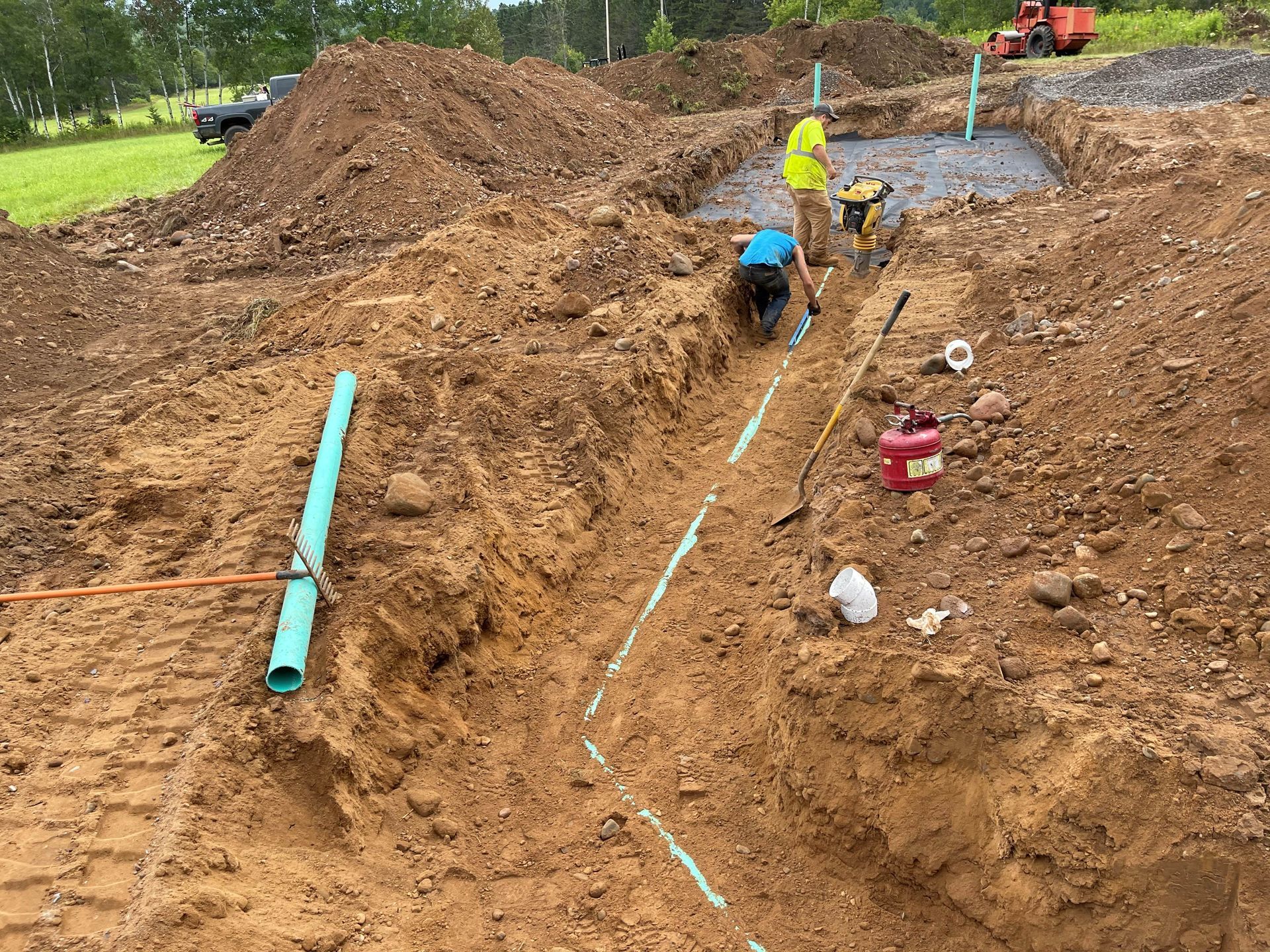 Two workers install utility pipes in a deep dirt trench at a construction site. Two workers install utility pipes in a deep dirt trench at a construction site.